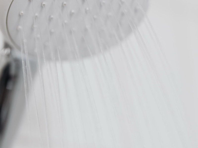 Regadera con agua corriendo en un baño con calentador de agua